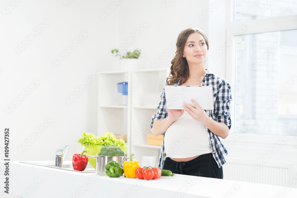Beautiful pregnant woman in the kitchen surfing in tablet Beautiful pregnant woman in the kitchen surfing in tablet