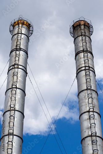 Two Gray Industrial Chimney Against The Blue Sky.
