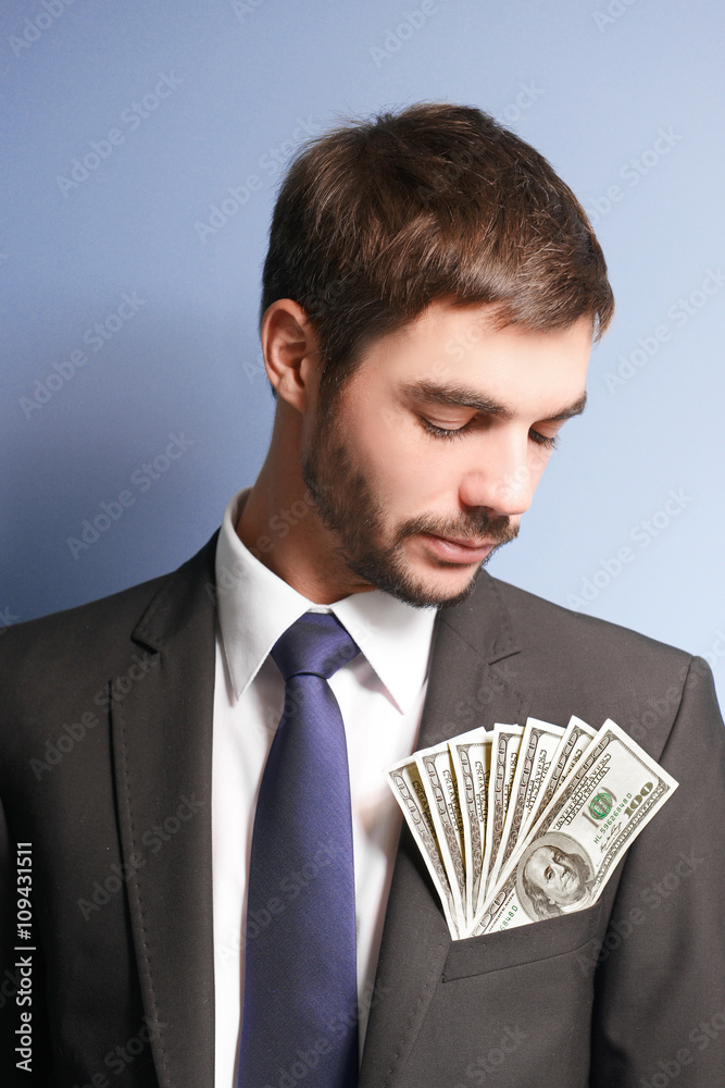 Attractive man in a suit with dollar banknotes in pocket on blue background Attractive man in a suit with dollar banknotes in pocket on blue background