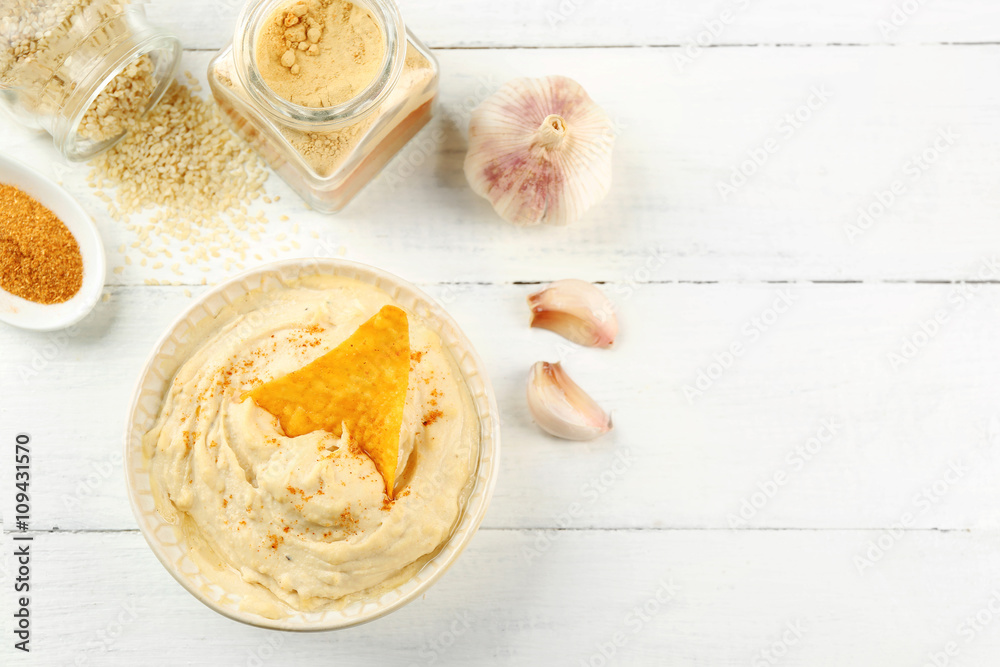 Ceramic bowl of tasty hummus with chips, spices and garlic on table Ceramic bowl of tasty hummus with chips, spices and garlic on table