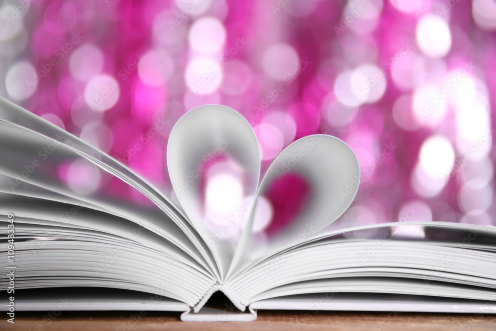 Sheets of book curved into heart shape on wooden table against unfocused lights Sheets of book curved into heart shape on wooden table against unfocused lights