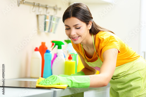 Beautiful woman in protective gloves cleaning electric range with rag