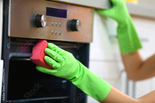 Woman hand in protective glove cleaning oven with sponge