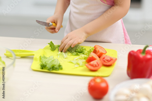 Little girl's hands cutting vegetables on a board.