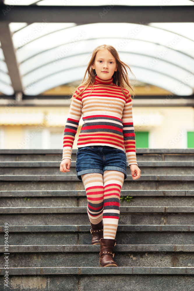 Fashion portrait of a cute little girl in a city, wearing brown boots,  denim shorts, stripes rollnecck pullover and tights Stock Photo