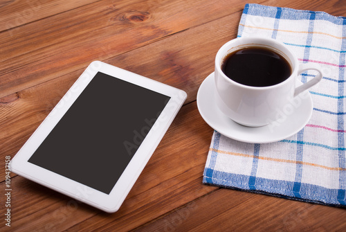 Digital tablet and coffee cup on a wooden table.