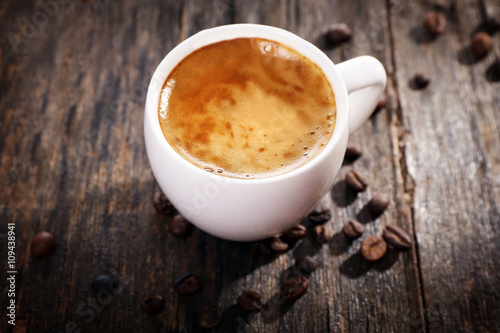 Cup of hot coffee with roasted beans on rustic wooden background