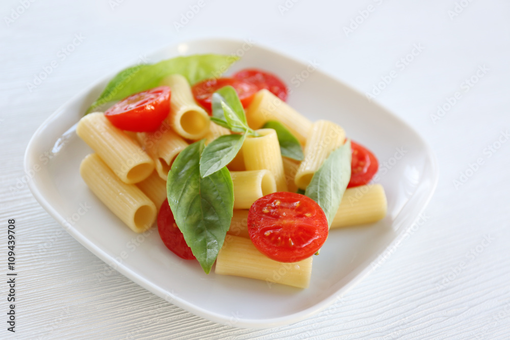 Boiled rigatoni pasta with fresh tomatoes and basil on white plate Boiled rigatoni pasta with fresh tomatoes and basil on white plate