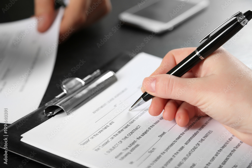 Female hand with pen signing contract at the desk closeup Female hand with pen signing contract at the desk closeup