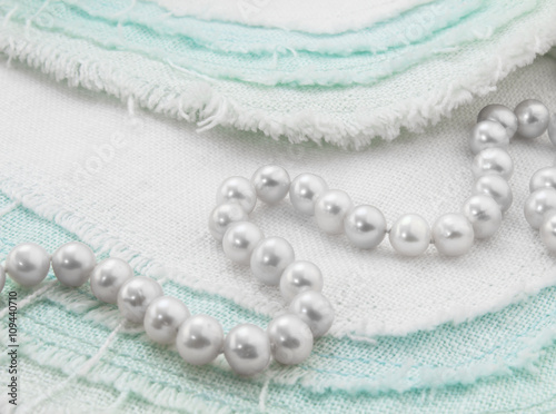 White pearl necklace closeup on turquoise and white frayed linen
