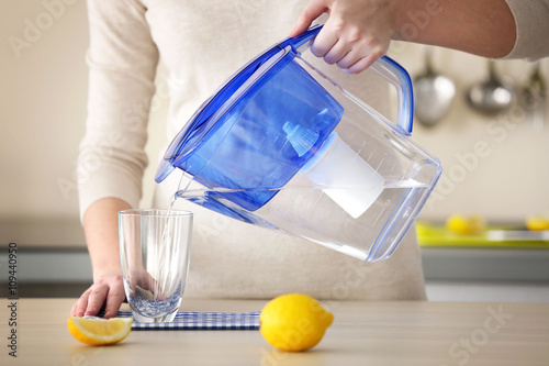 Woman pouring water from filter jug into glass in the kitchen