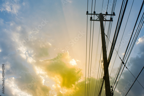 Silhouette, Pole with power lines lies across. The light shines in the evening sky backdrop, with space.