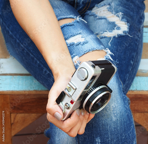 Stylish women sitting in torn jeans with old camera. Fashion, lifestyle, beauty, clothing.
