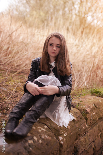 Beautiful teenage girl sitting on a stone wall looking into the distance