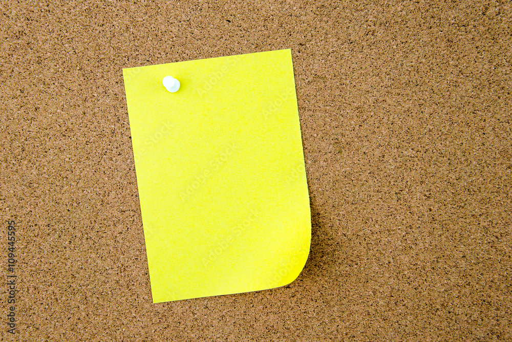 Blank yellow paper note pinned on cork board Blank yellow paper note pinned on cork board