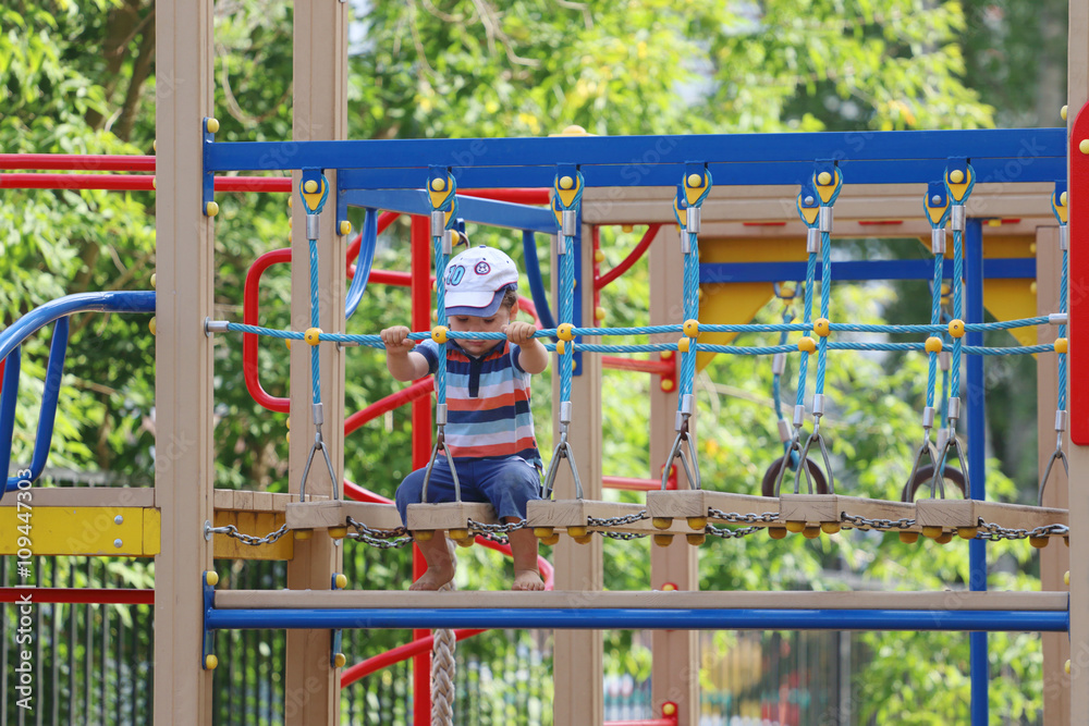 Little barefoot boy sits on playground and plays at summer day