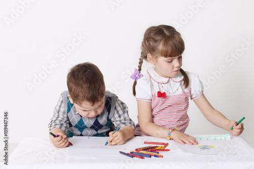 Little boy and girl draw with crayons sitting at table