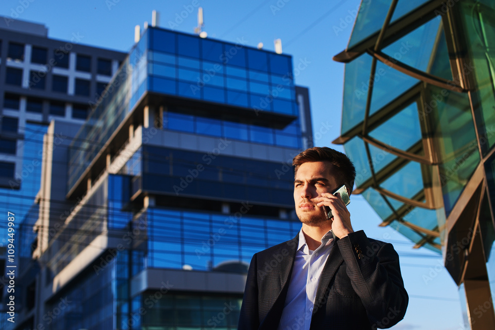 Man in suit talking on mobile phone against the building with a glass facade Man in suit talking on mobile phone against the building with a glass facade