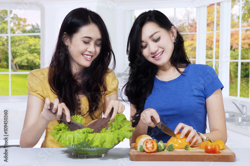 Asian women preparing salad in kitchen