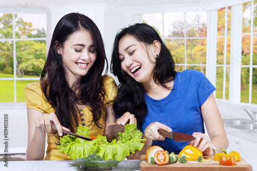 Happy women cooking salad in kitchen