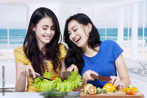 Two cheerful girls making salad
