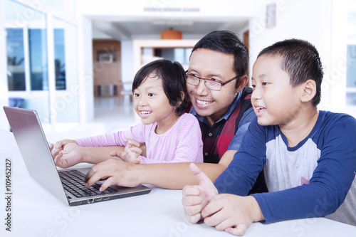 Two kids using laptop with dad at home © Creativa Images