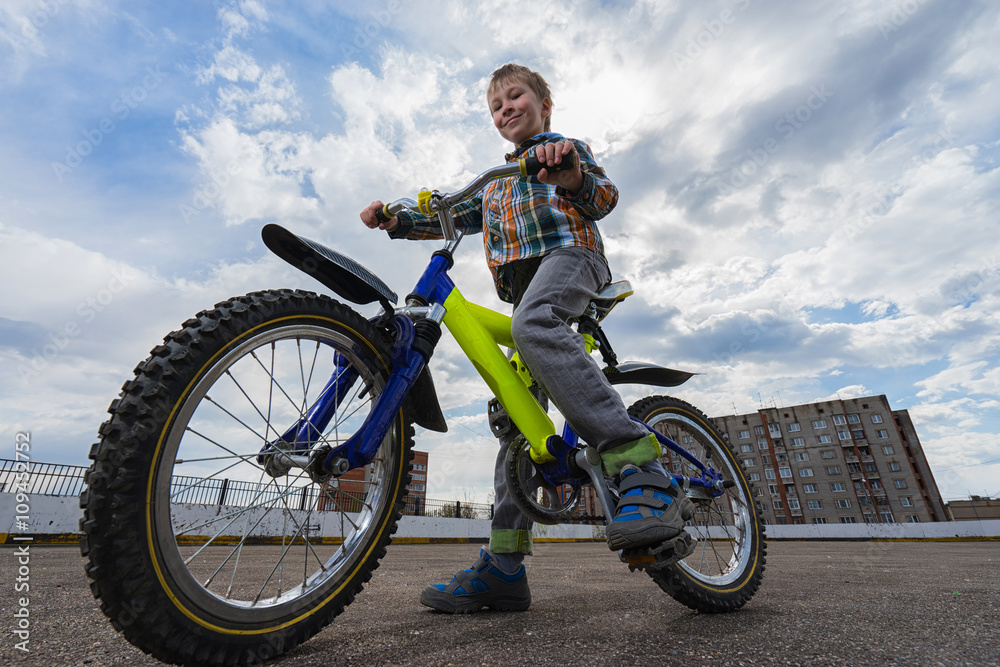 Obraz premium Urban biking - small happy boy and bike in city. Focus on boy