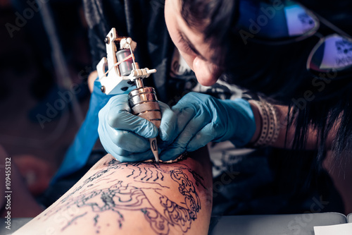 Close up tattoo artist demonstrates the process of getting black tattoo with paint. Master works in black sterile gloves. Master of tattoo fill circuit tattoo.