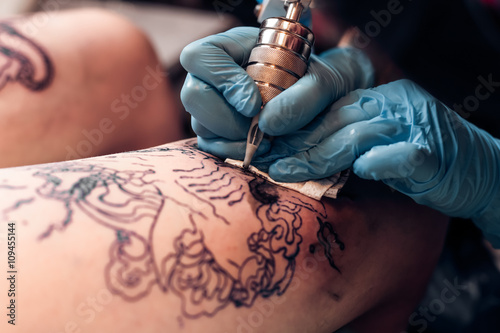 Tatuaż artysta wypełnić tatuaż obwodu w profesjonalnym salonie. Noga z wzorem i czarną farbą. Mistrz pracuje w czarnych sterylnych rękawiczkach.