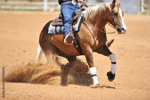 A side view of a rider and horse running ahead in the dust.