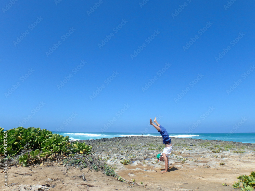 Man Handstanding on coral rocks on the beach as wave crash in th