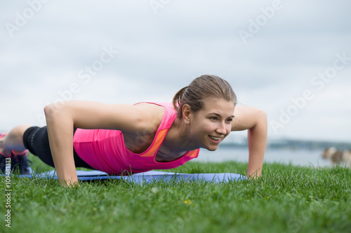 Fotografie Young woman doing push up exercises outdoor