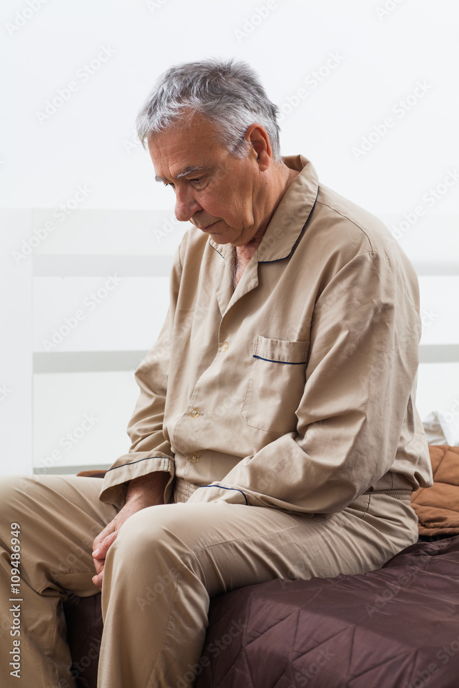 Worried senior is waking up. He is sitting on bed ready to get up. Worried senior is waking up. He is sitting on bed ready to get up.