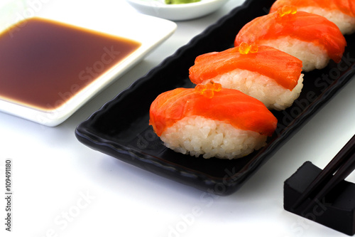 Salmon Sushi on the black plate on a white table.