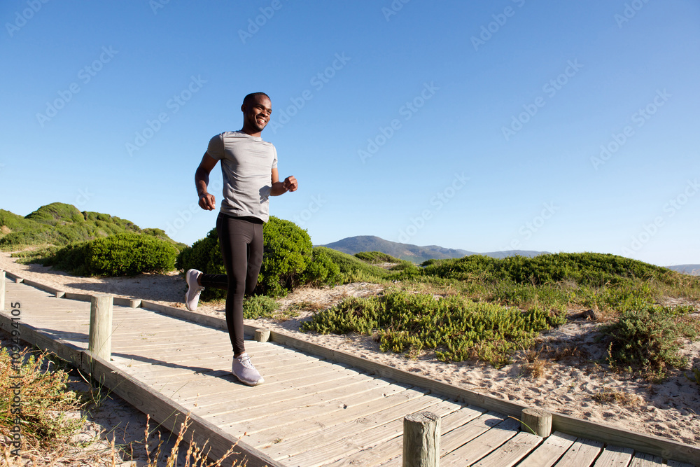 Healthy young african man running on boardwalk at the beach