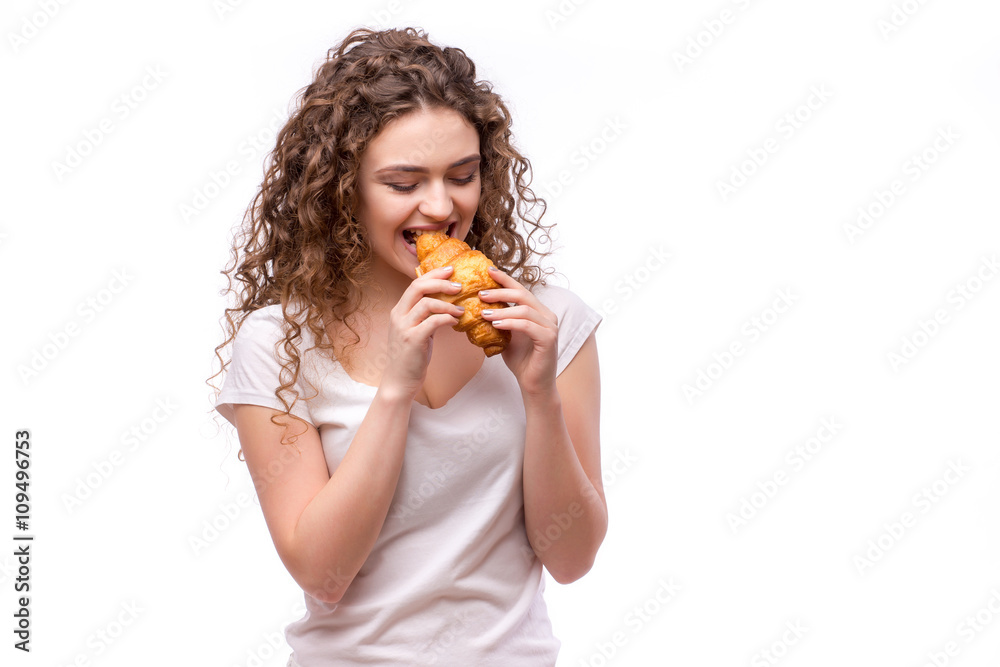 Curly woman eating a croissant on isolated background Curly woman eating a croissant on isolated background