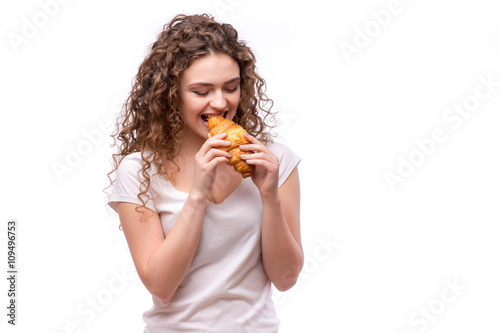 Curly woman eating a croissant on isolated background