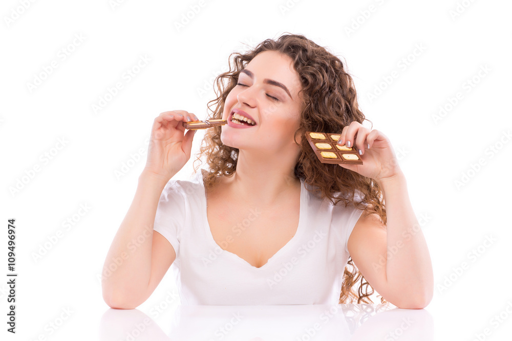Curly young woman with plate of milk chocolate at table. Concept of diet. Curly young woman with plate of milk chocolate at table. Concept of diet.