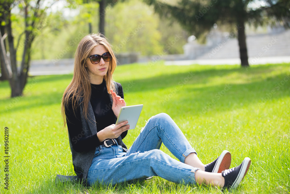 Beautiful girl sitting on the grass with the tablet. Beautiful girl sitting on the grass with the tablet.