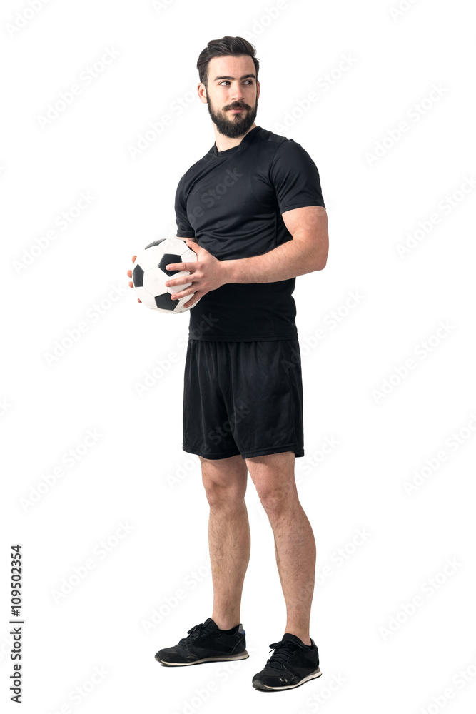 Fototapeta premium Strong confident soccer player holding ball with both hands looking away. Full body length portrait isolated over white background.