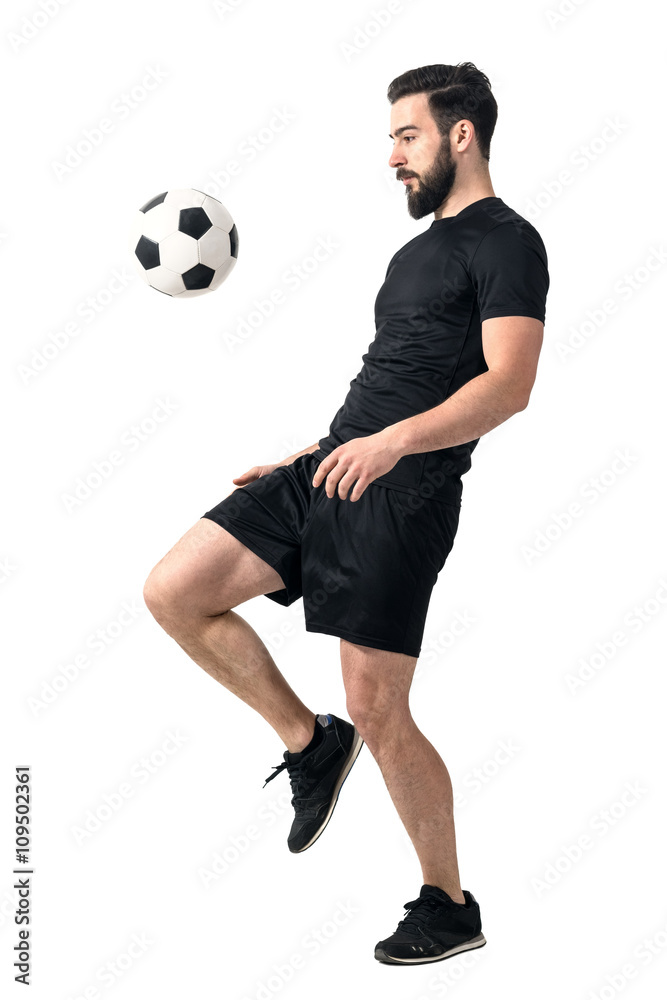 Fototapeta premium Side view of football or futsal player juggling ball with his knee. Full body length portrait isolated over white background.