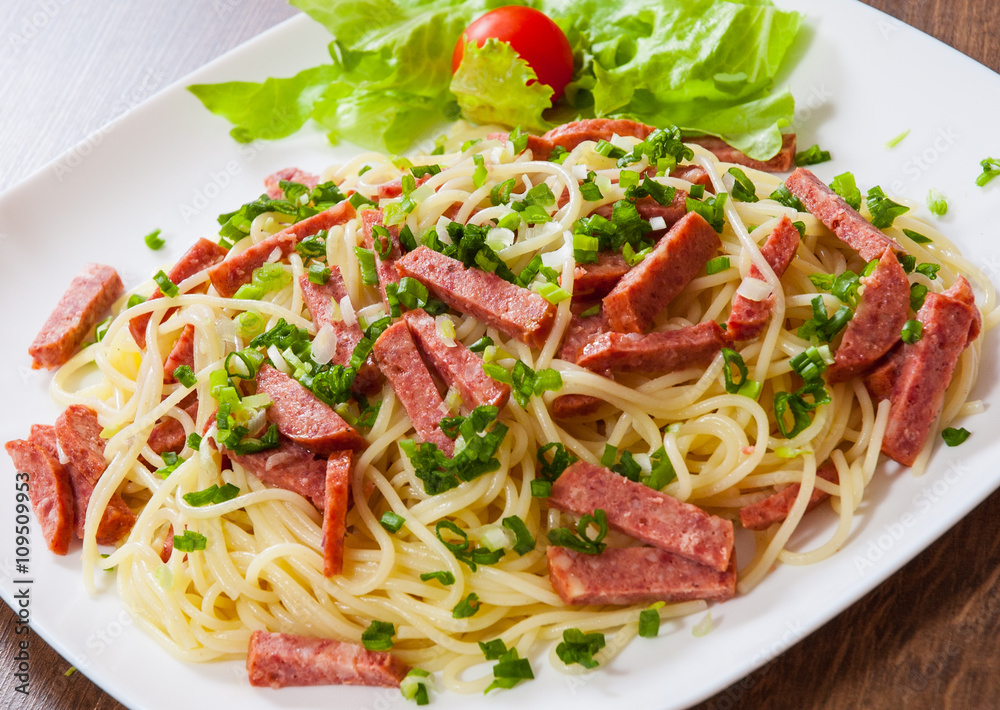 spaghetti pasta with salami sausage in a plate on wooden table spaghetti pasta with salami sausage in a plate on wooden table