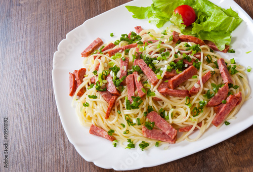 spaghetti pasta with salami sausage in a plate on wooden table