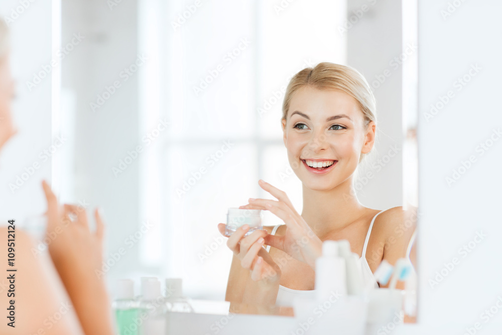 happy woman applying cream to face at bathroom happy woman applying cream to face at bathroom