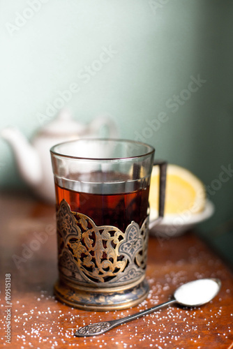 Cup of tea in antique glass-holder with sugar, lemon and teapot. Vintage concept.