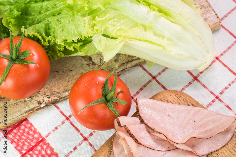 Ingredients for sandwich -tomatoes, lettuce and pieces of ham.