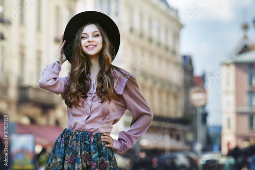 Outdoor portrait of a young beautiful fashionable happy lady posing on a street of the old city. Model wearing stylish clothes. Girl looking at camera. Female fashion. City lifestyle. Copy space