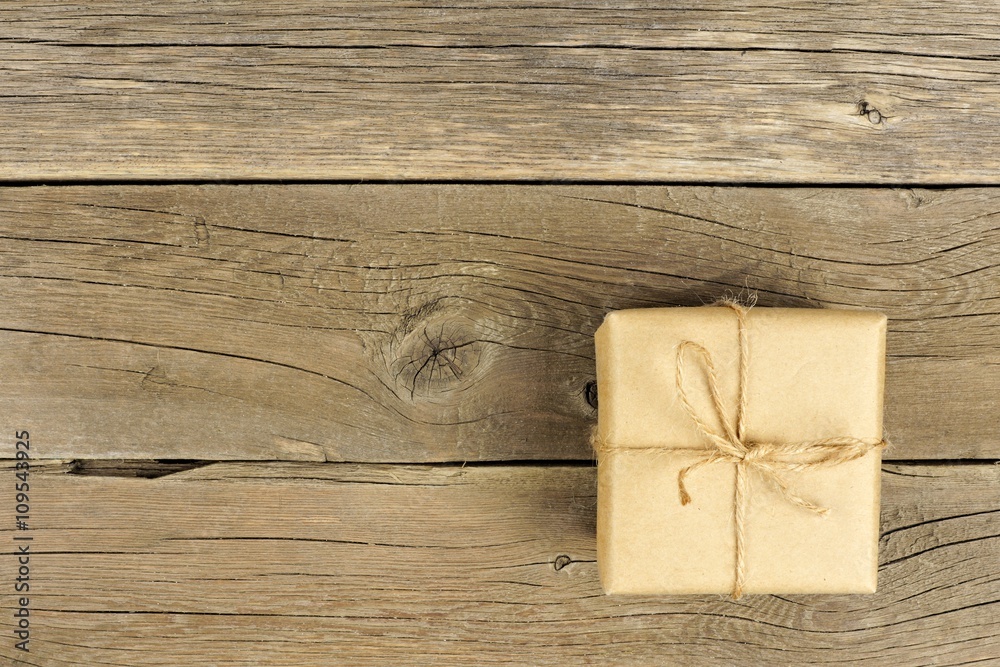 Brown paper wrapped gift box with twine bow on a rustic wood background Brown paper wrapped gift box with twine bow on a rustic wood background