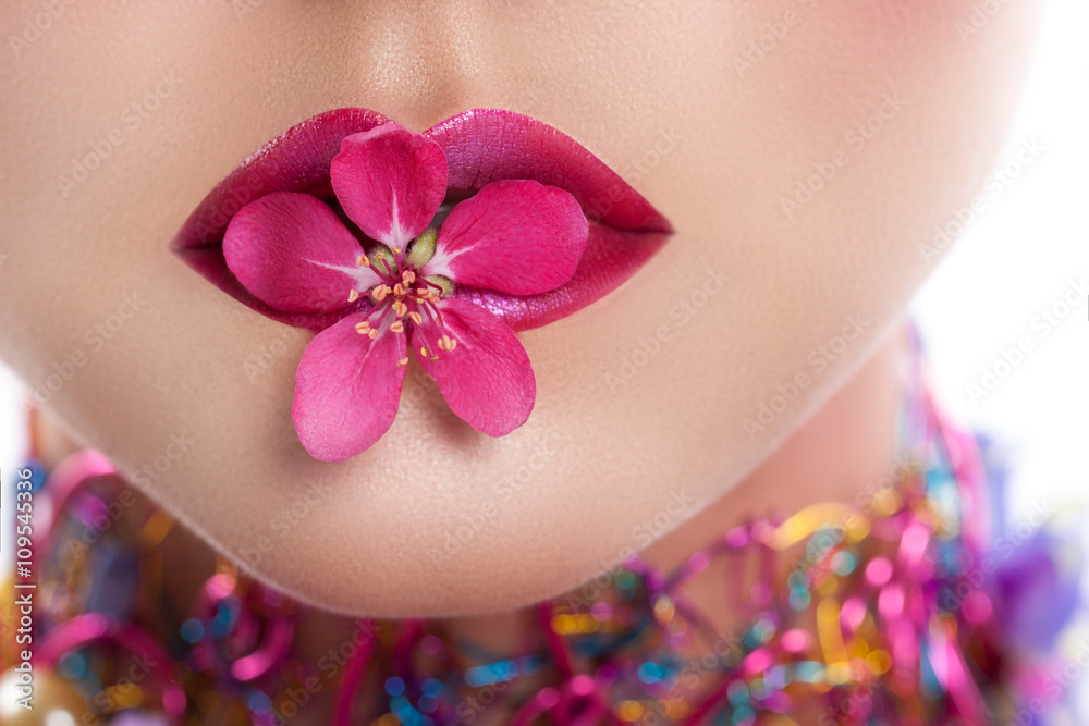 female lips closeup. A girl holding a flower in her lips. Perfect make-up to red-violet lipstick female lips closeup. A girl holding a flower in her lips. Perfect make-up to red-violet lipstick