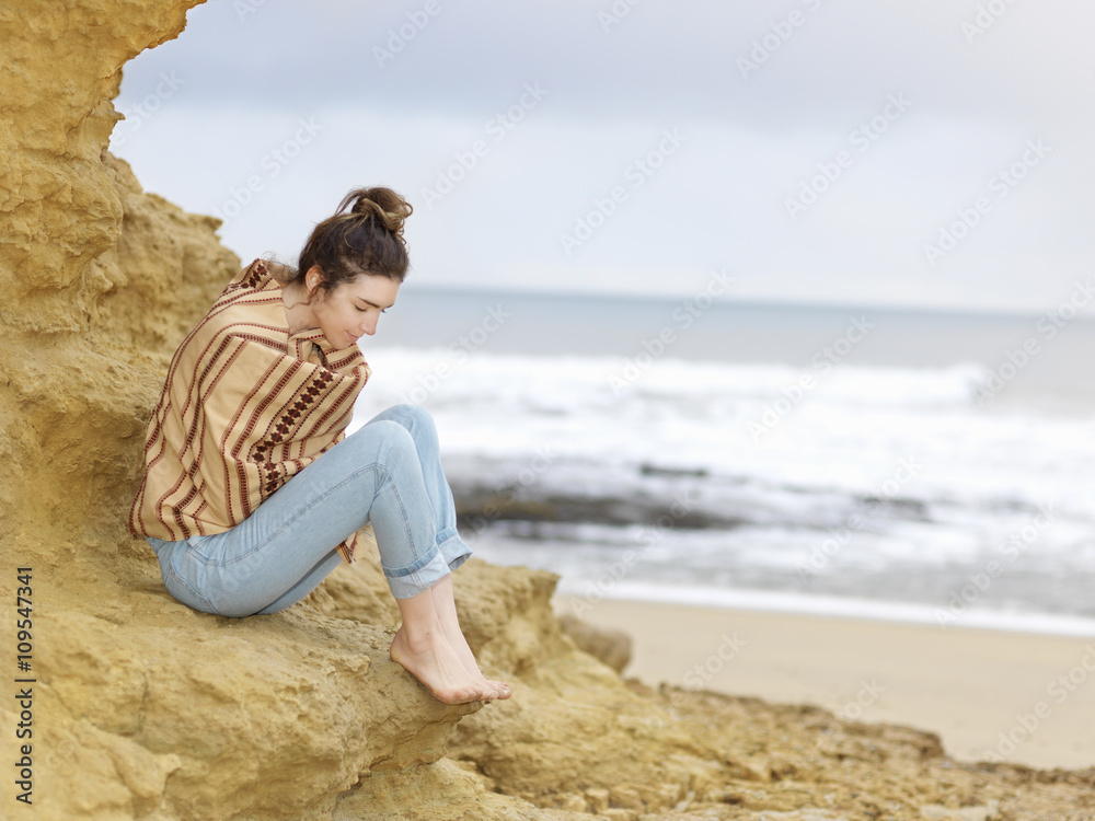 Young woman wrapped in shawl sitting on cliffside, Point Addis, Anglesea, Victoria, Australia Young woman wrapped in shawl sitting on cliffside, Point Addis, Anglesea, Victoria, Australia